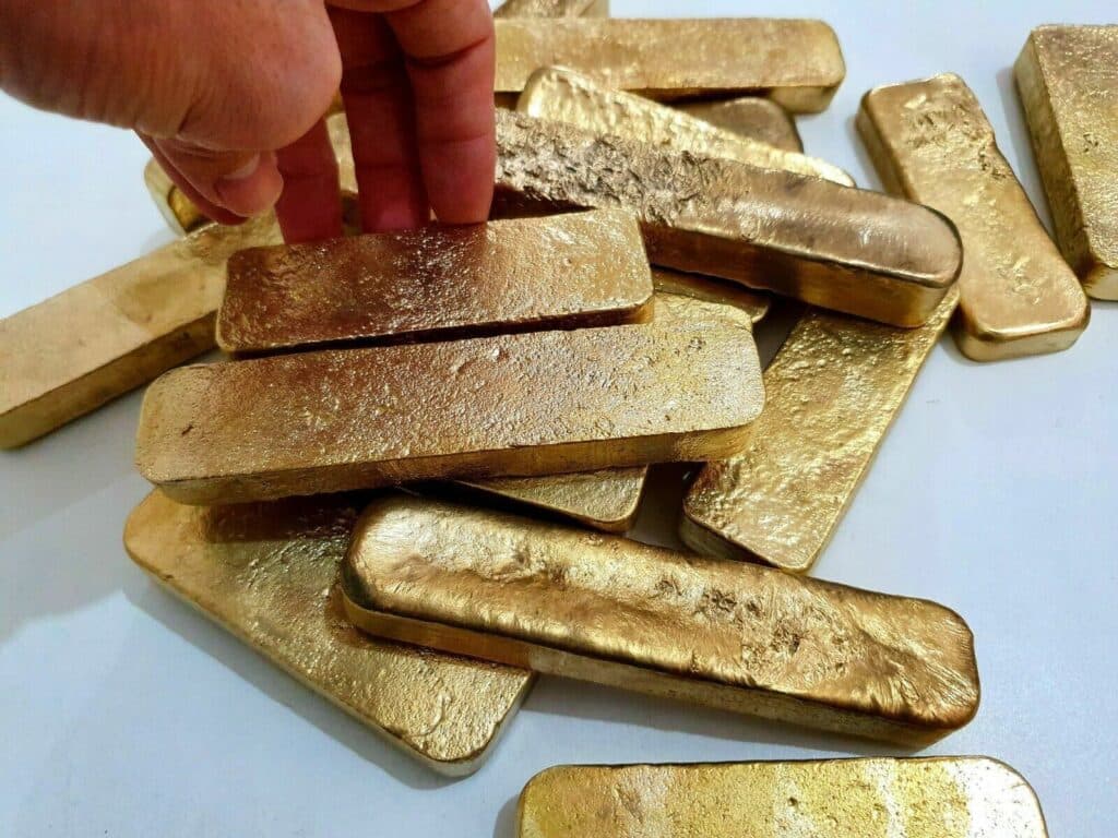 Close-up of unrefined gold dore bars being handled, showcasing raw gold form before final refining.
