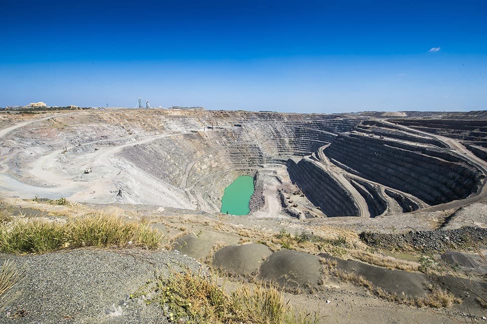Large open pit gold mining operation showing terraced excavation and a green water pool, illustrating where gold is found.