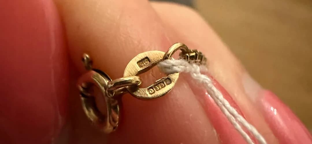 Close-up image of a necklace clasp showing a 375 gold hallmark and 375 stamp, indicating the item is made from 9 carat gold (37.5% purity).