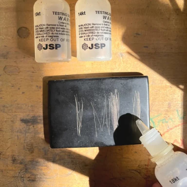 Image of a home gold testing kit in use, featuring 10kt, 14kt, and 18kt acid solutions and a black gold touchstone marked with test scratches—illustrating how to test gold at home.