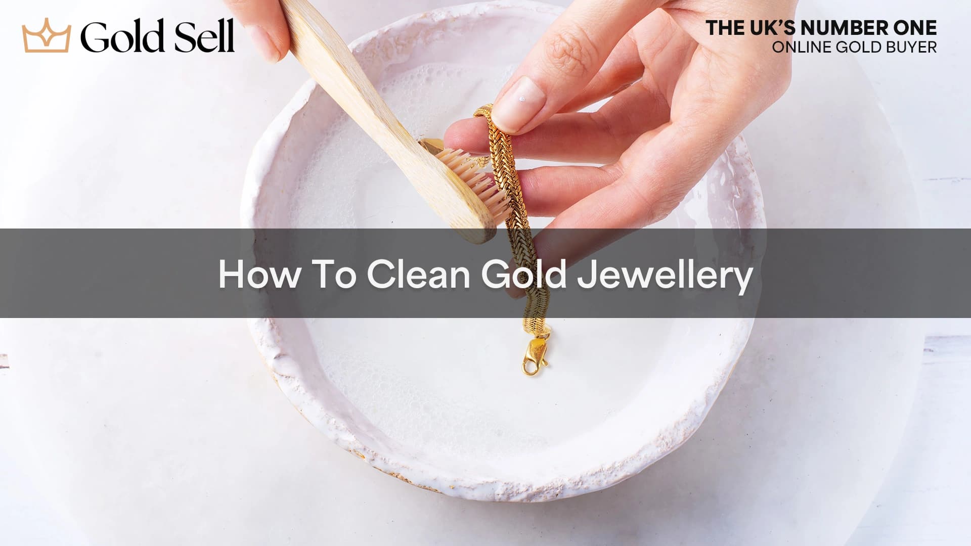 Hands gently scrubbing a gold bracelet in a bowl of soapy water with a soft toothbrush, illustrating how to clean gold jewellery at home.