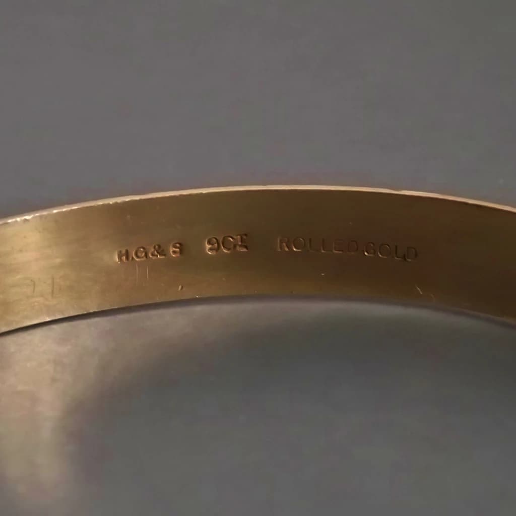 Close-up of a vintage rolled gold hallmark reading “H.G&S 9CT ROLLED GOLD”, indicating the item is coated with 9-carat gold using the rolled gold method.