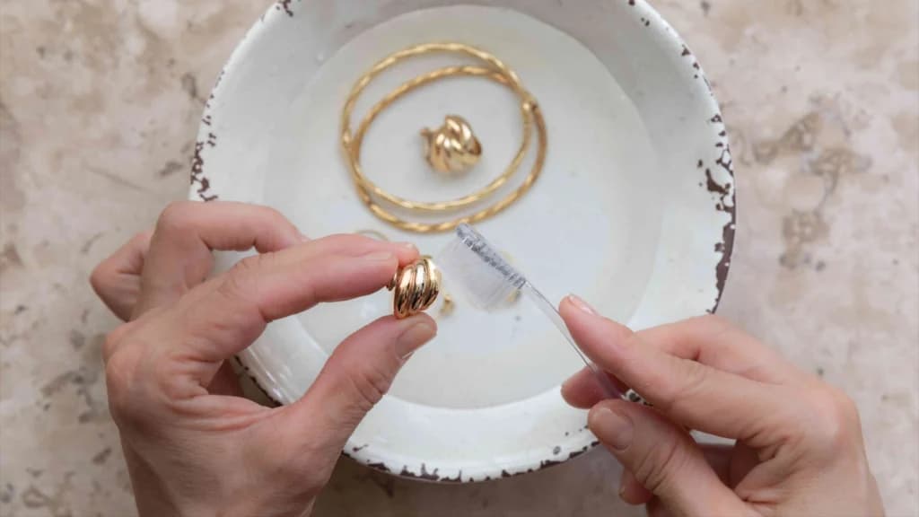 Close-up of hands using a toothbrush to untarnish gold, demonstrating how to clean gold at home safely and effectively.