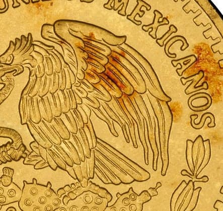 Close-up of red spots on gold coin showing surface oxidation caused by trace copper impurities in the alloy.